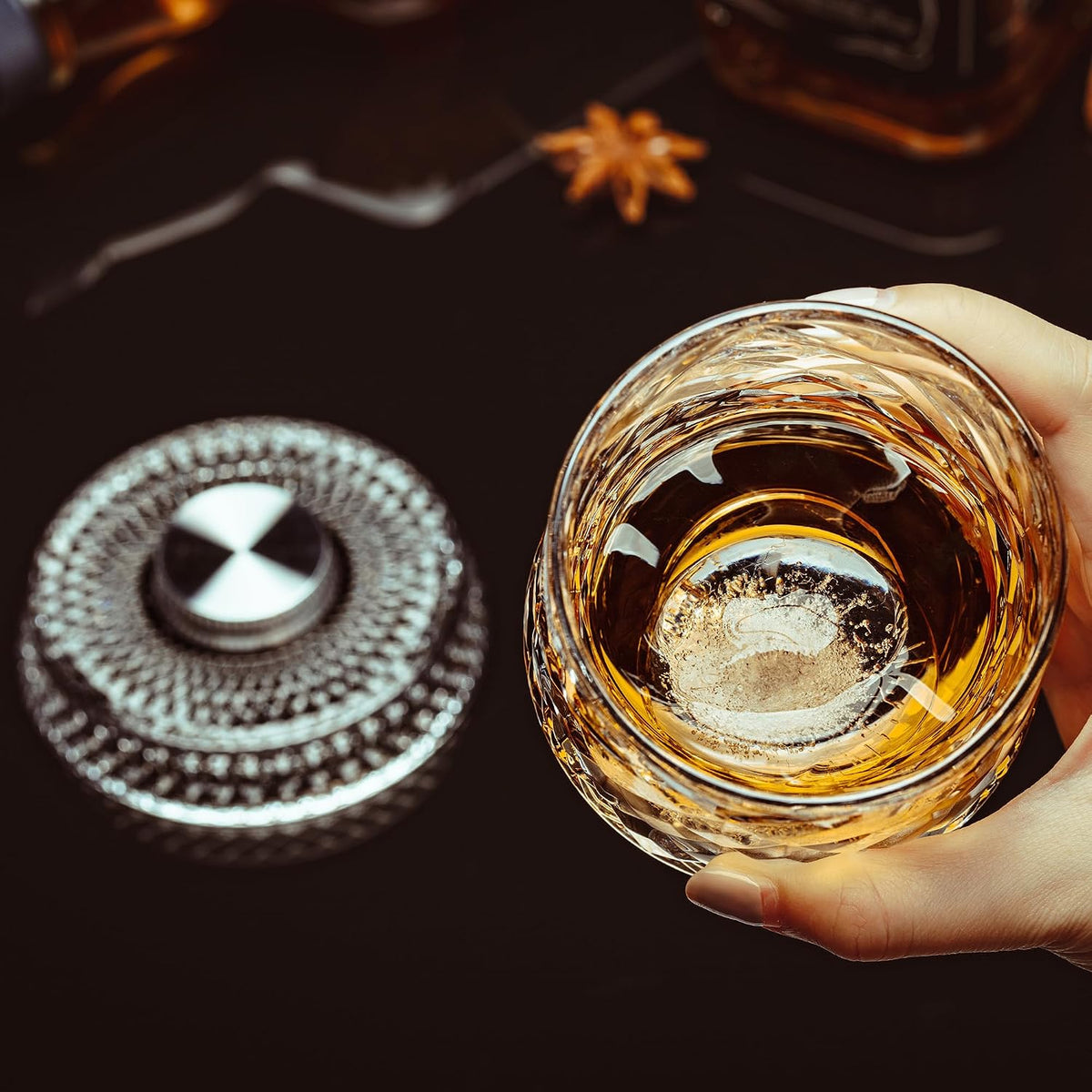 Spinning crystal whiskey glass with an ice sphere beside its rotating base